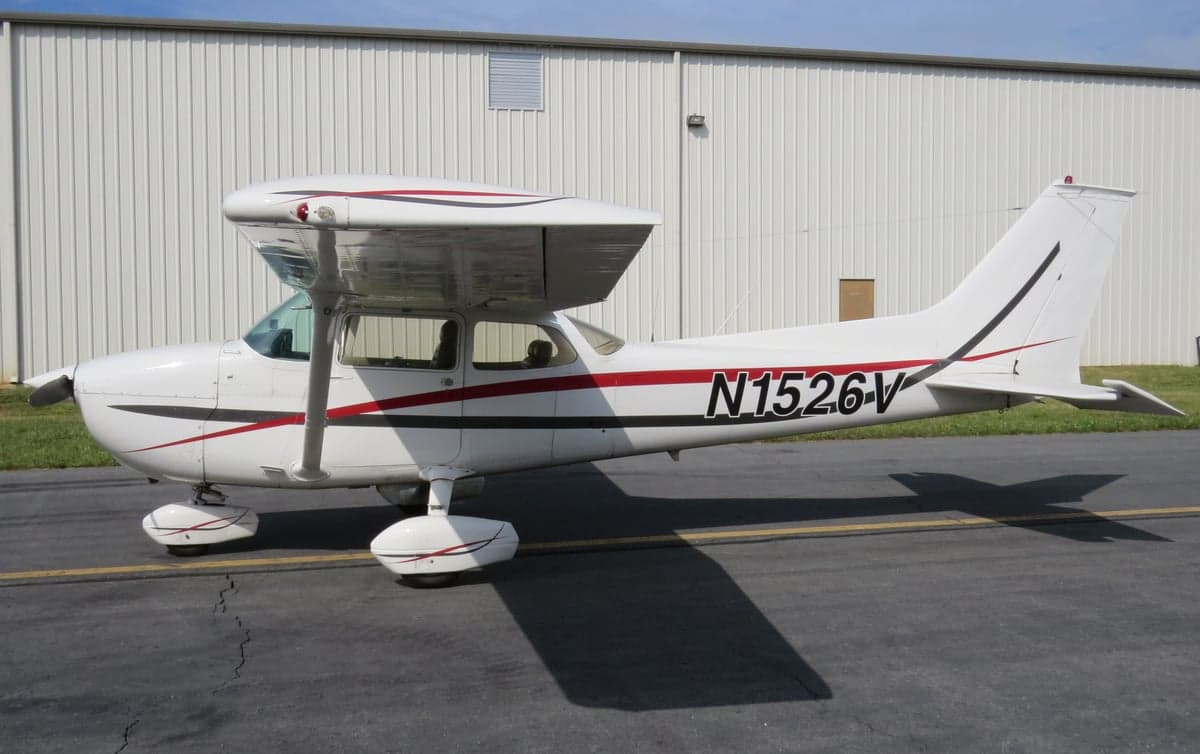 Side view of a white and red Cessna 152 with registration N1526V parked on the tarmac.
