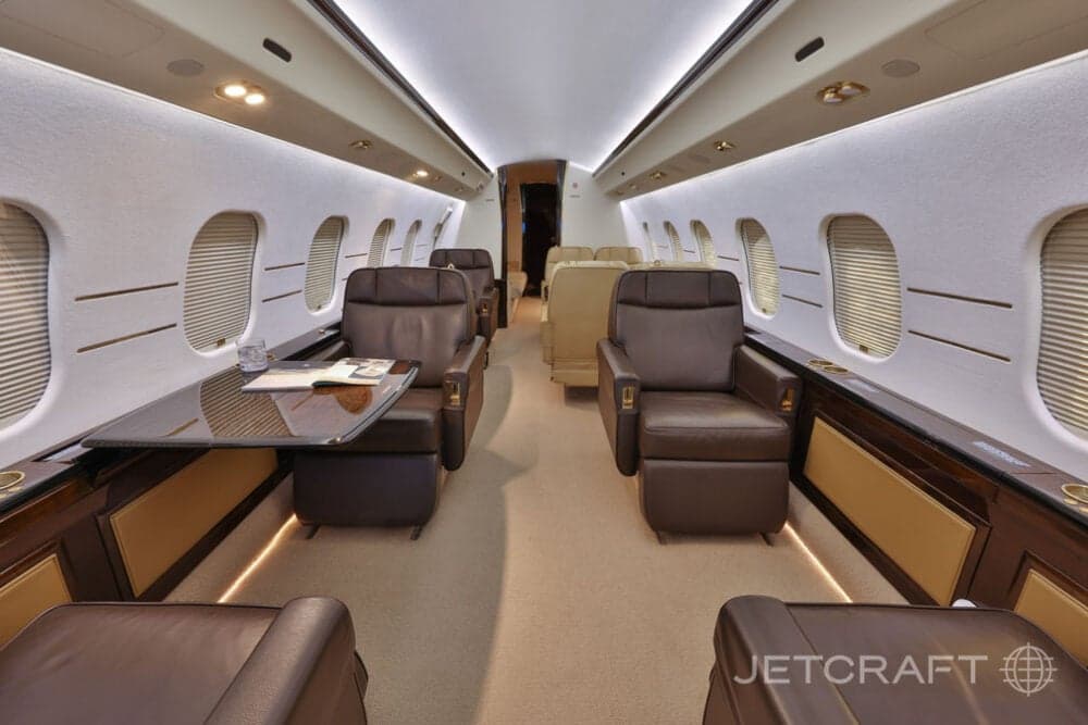 The luxurious cabin interior of a business jet, featuring brown leather seats and a dark wood table.