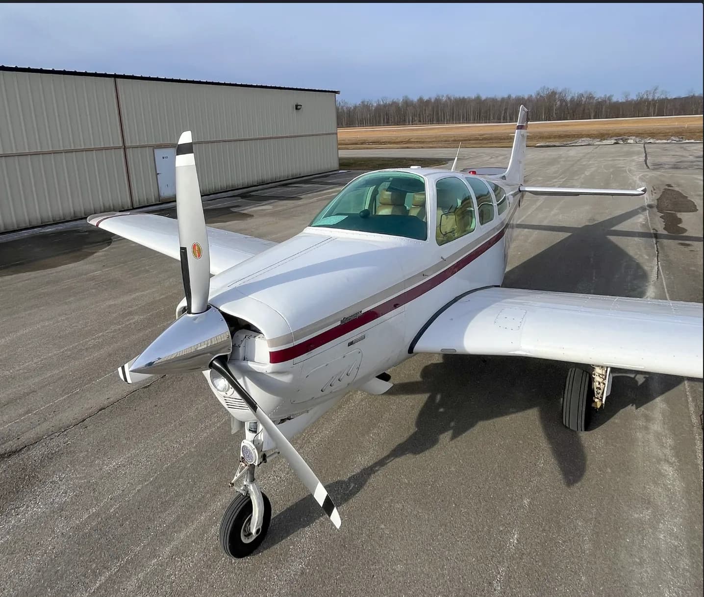 An elevated front-quarter view of a white and maroon Beechcraft Bonanza aircraft on a tarmac.