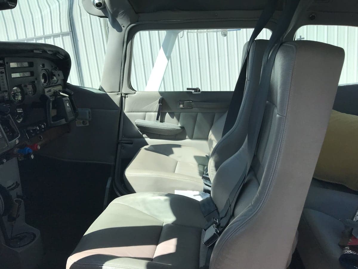 The light gray interior cabin of a small aircraft, showing the front seats and a partial view of the cockpit on the left.