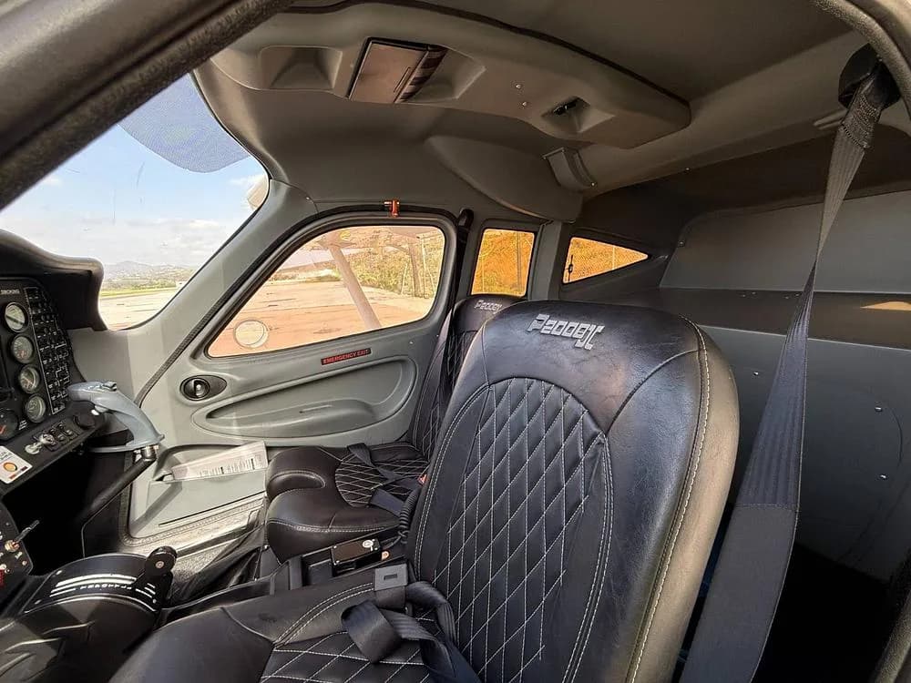 The interior cabin of a Tecnam P2008, showing black leather seats with white stitching and the side panel.