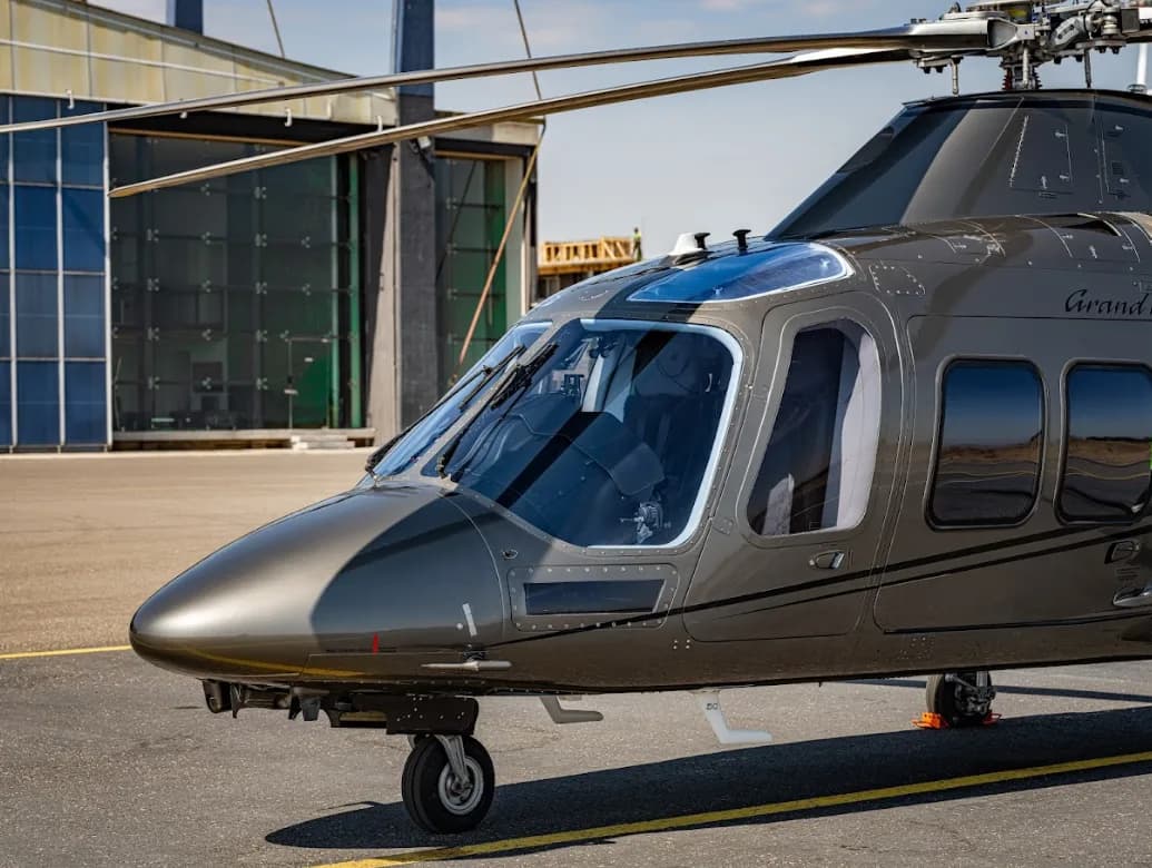 A close-up view of the nose and cockpit windows of a grey AgustaWestland AW109 GrandNew helicopter.