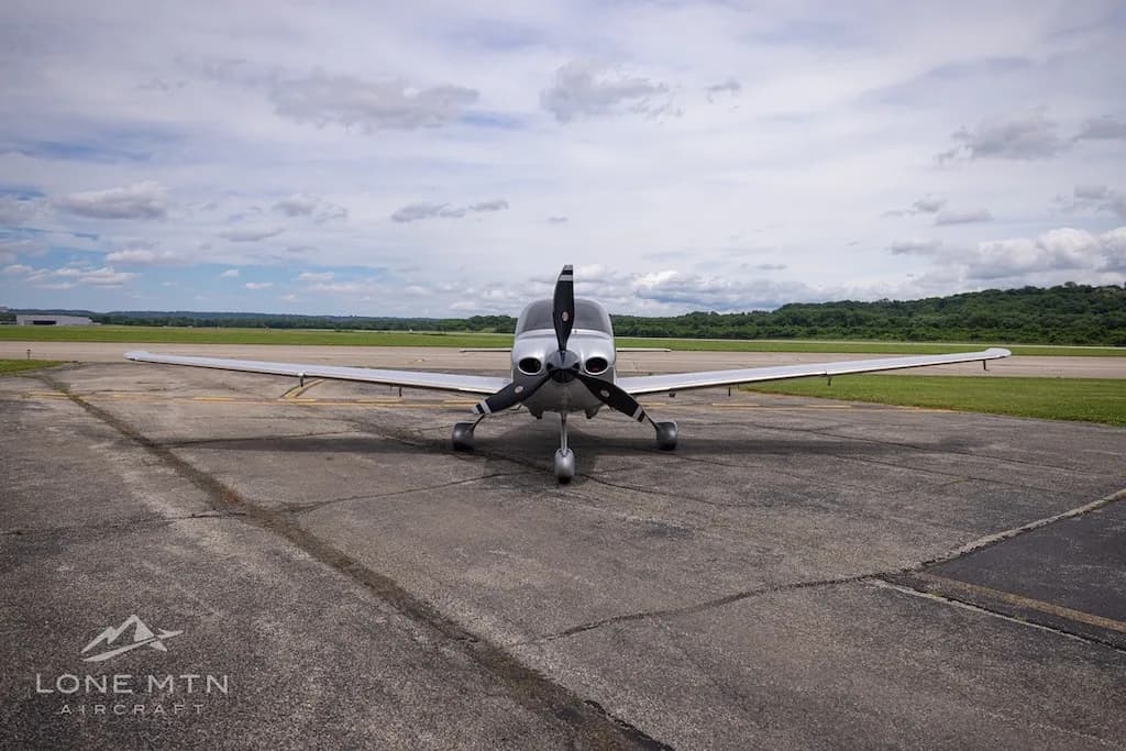 A front view of a silver and blue Cirrus SR22T Carbon aircraft parked on an airfield.