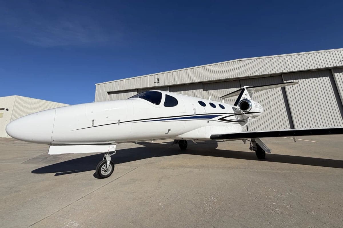 A Citation Mustang aircraft parked on the tarmac in front of a hangar, side view.