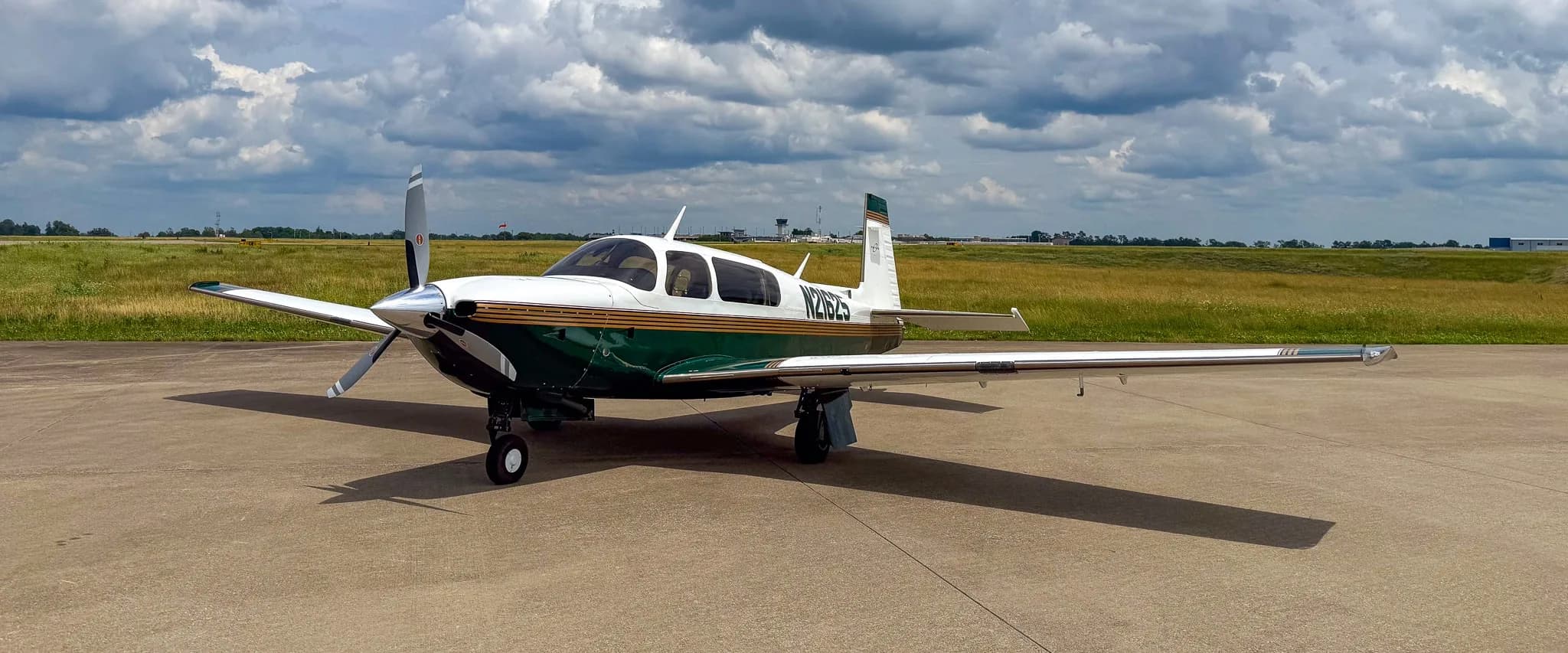 A white and green Mooney M20 aircraft with registration N21625 parked on an airfield under a cloudy sky.