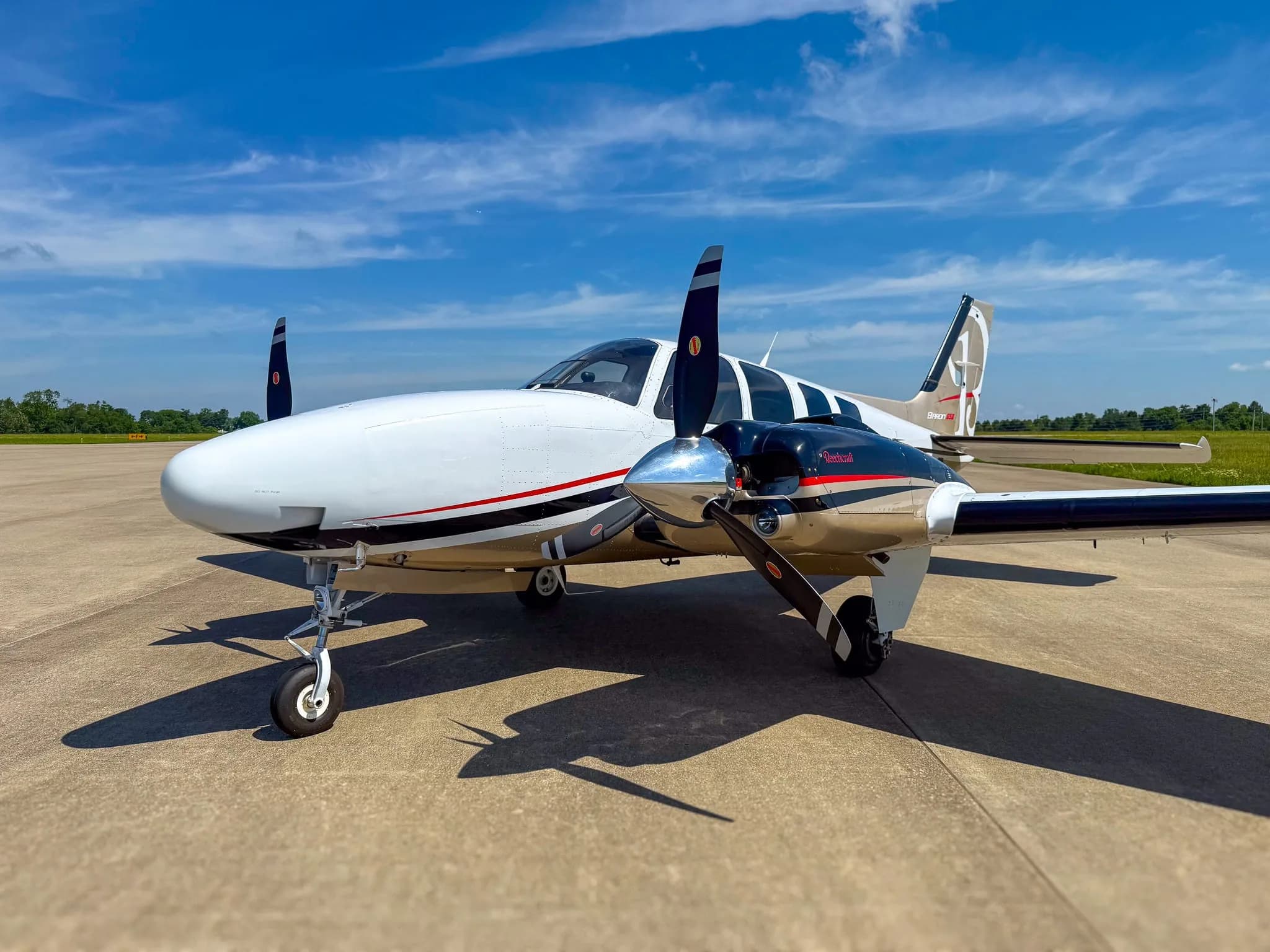 Front right side view of a white and gold twin-engine Beechcraft Baron G58 on an airfield.