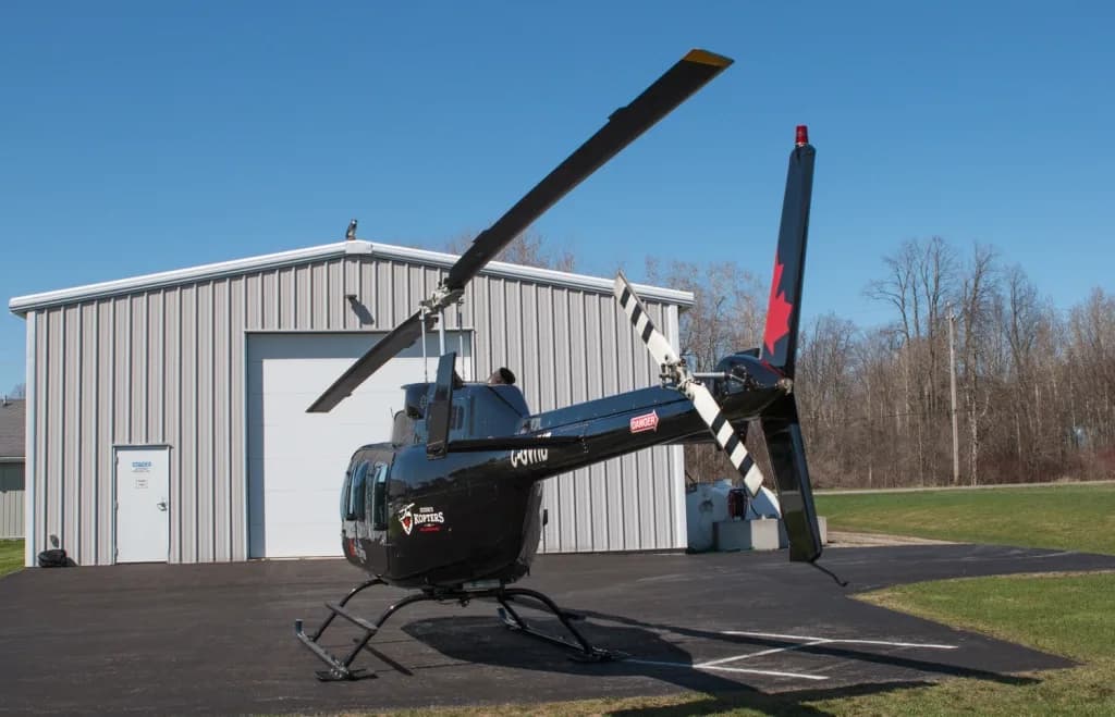 A rear view of a black Bell 206 helicopter with registration C-GVHD parked in front of a white hangar.