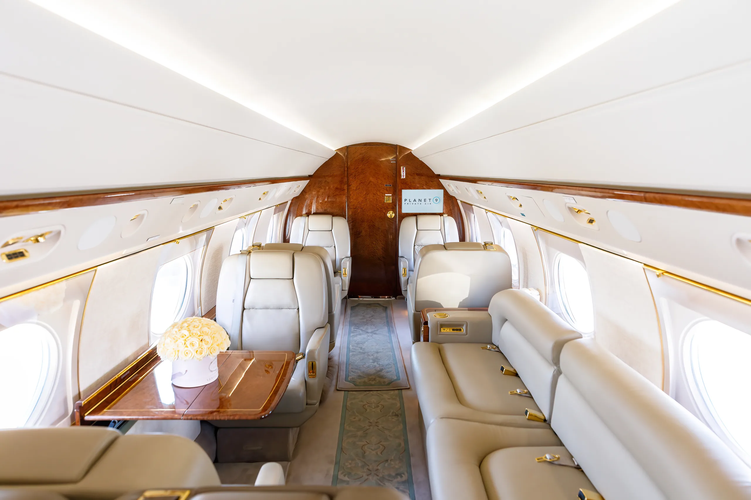 A spacious aircraft cabin with light leather seating, wood trim, and a bouquet of white roses on a table.