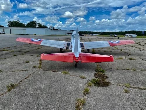 Rear view of a red and white aircraft with British markings on a cracked concrete runway.