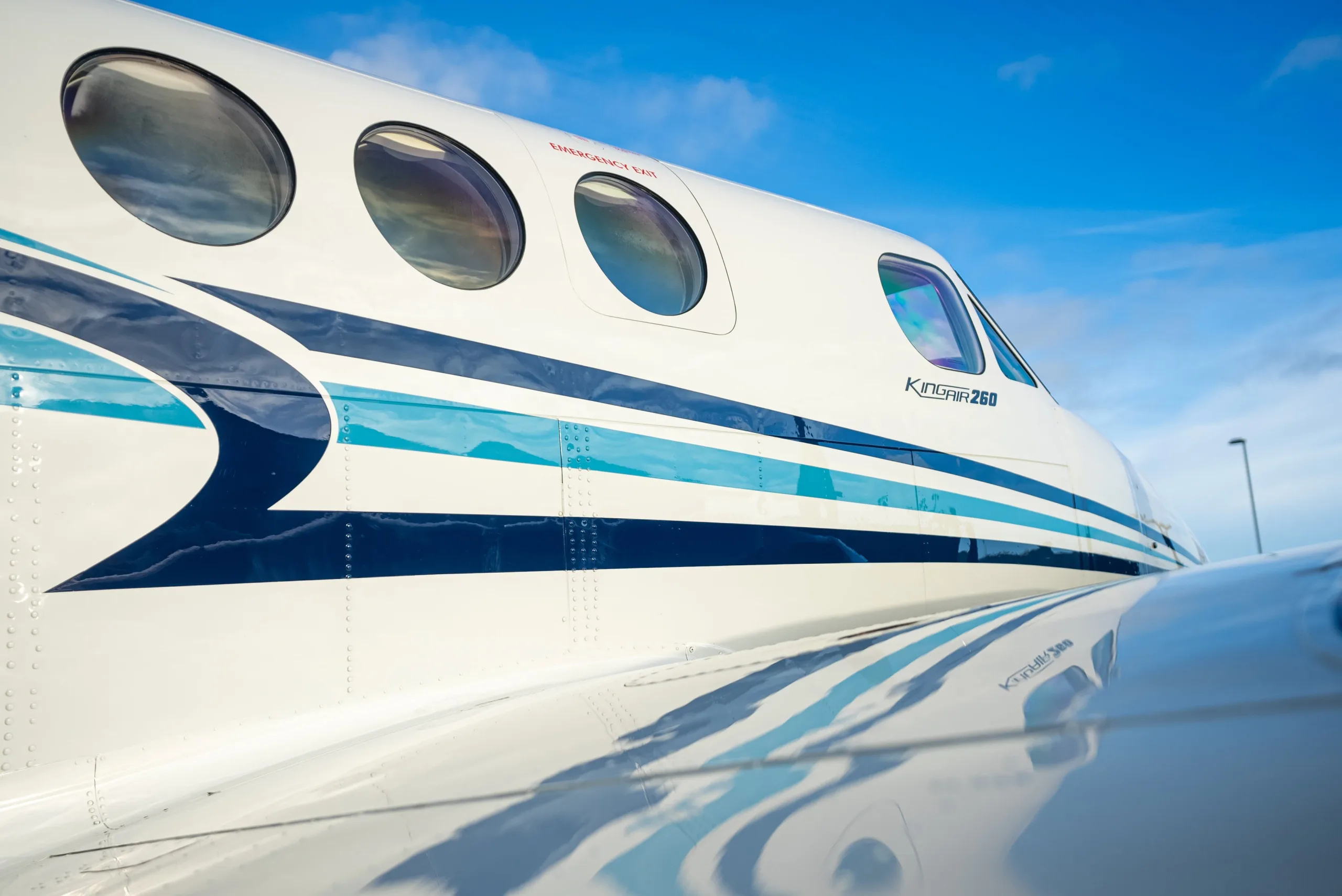 A close-up side view of the white and blue fuselage of a Beechcraft King Air 260, showing the aircraft type and windows.