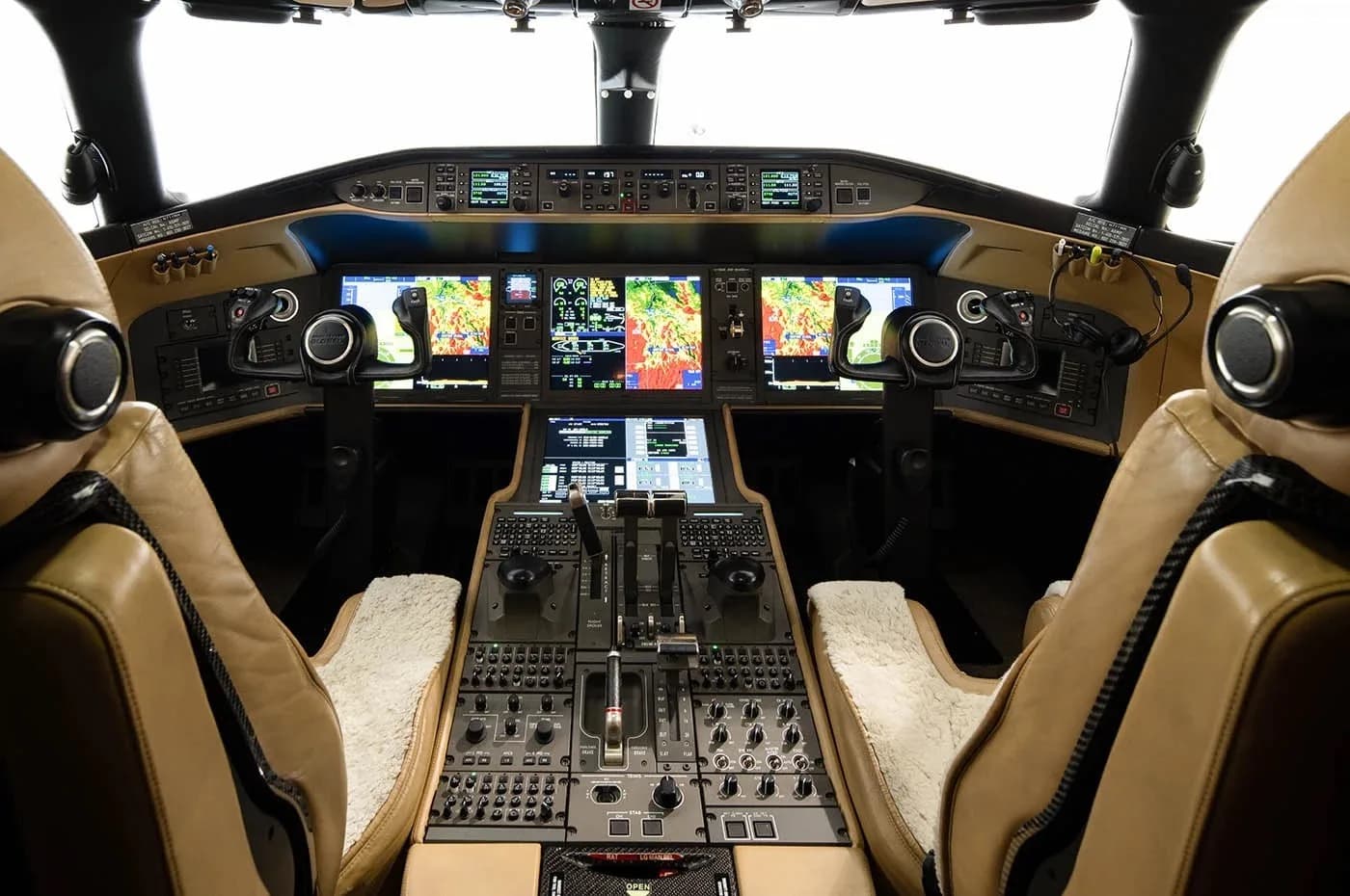 The modern cockpit of a business jet features multiple digital displays and tan leather pilot seats.