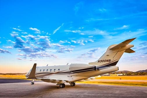 A rear-side view of a white business jet with dark and gold stripes, registration N300NB, parked on a tarmac.