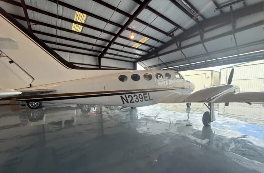 A close-up side view of the white Cessna 414 aircraft with gold and black stripes and registration N239EL, parked in a hangar.