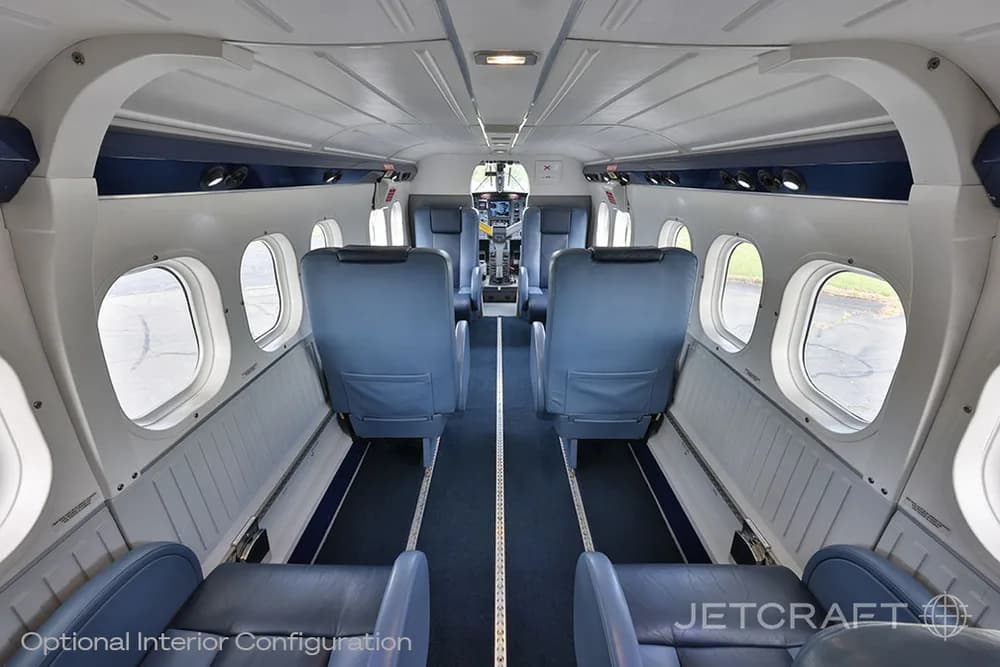 A view down the aisle of an aircraft cabin with blue seats and the cockpit visible in the distance.