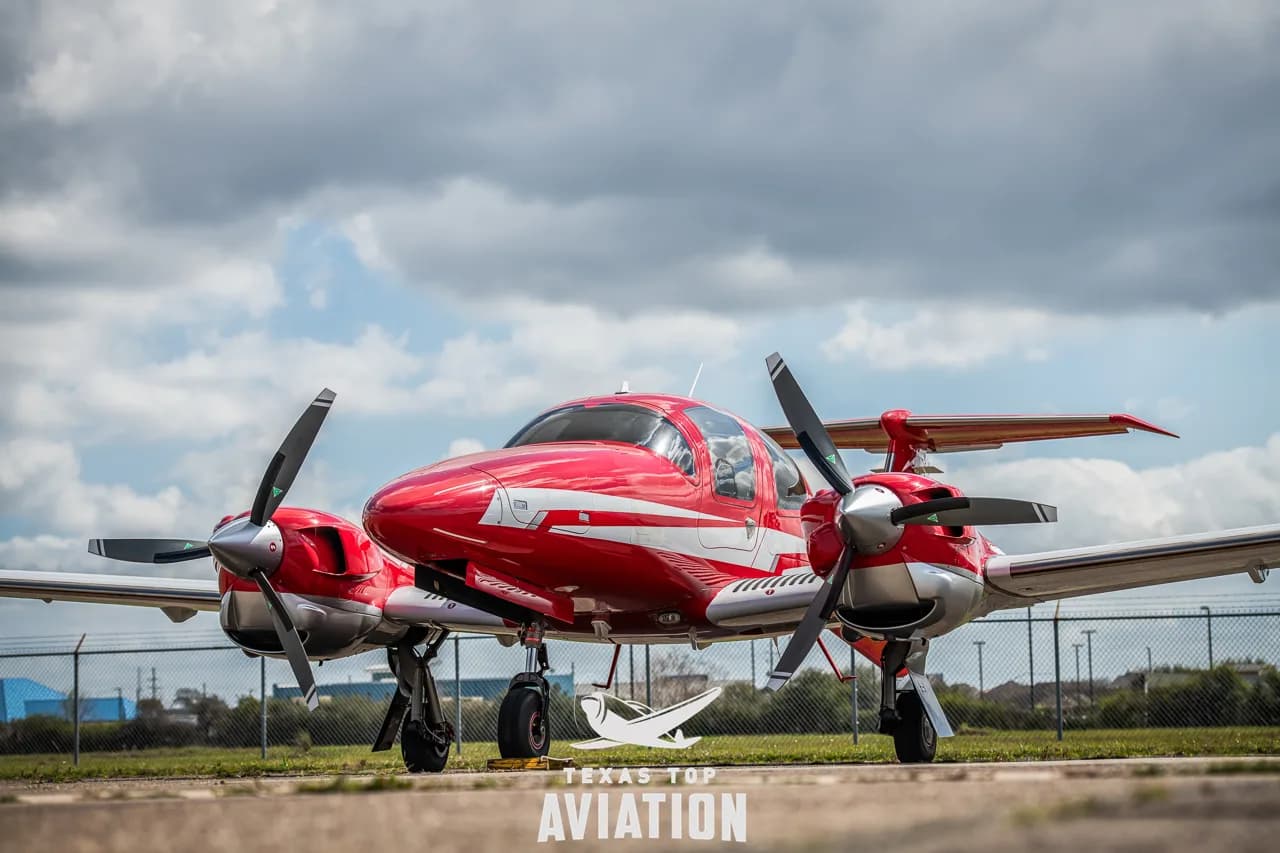 A red and white Beechcraft Baron aircraft is parked on the tarmac.