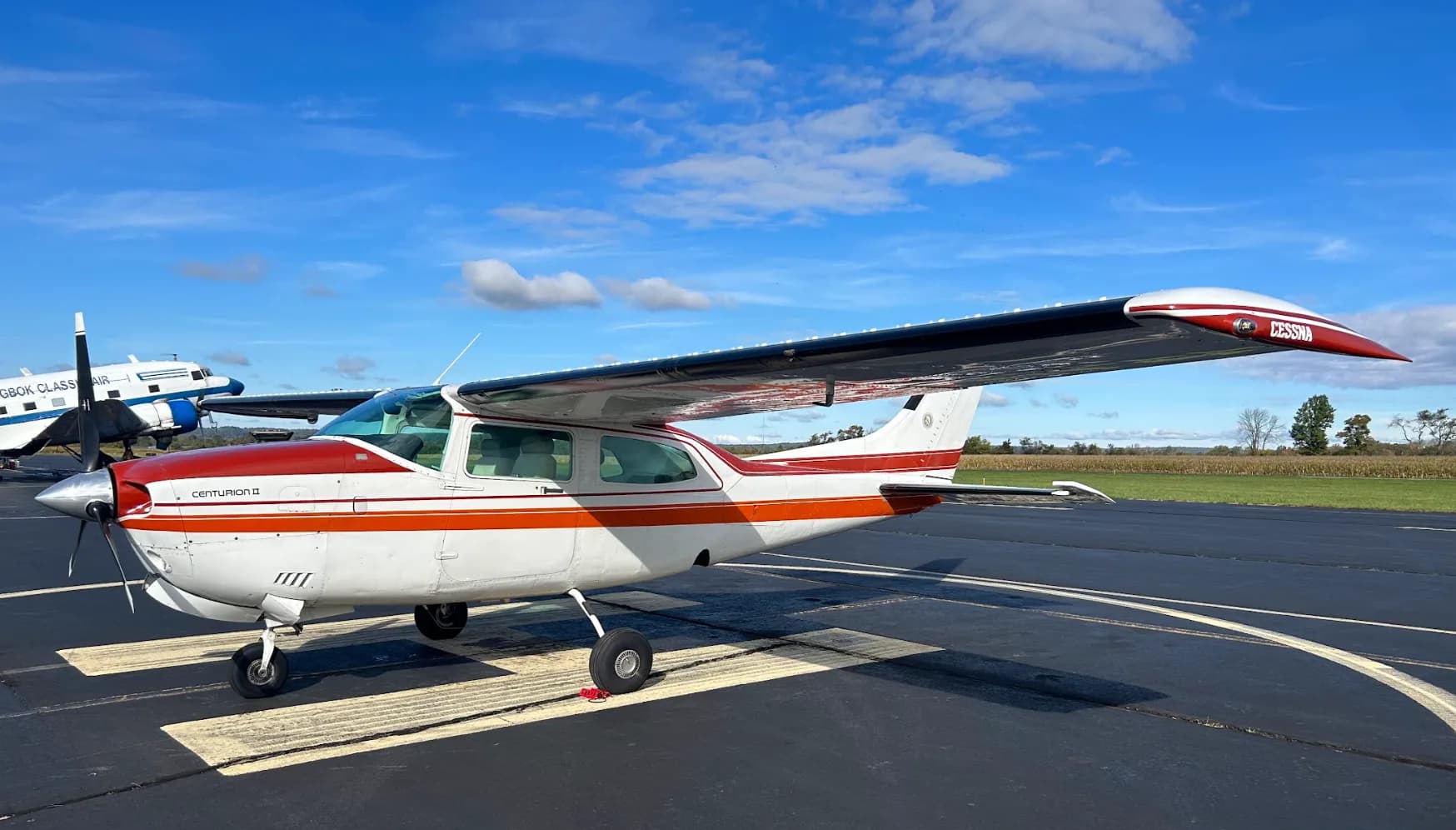 A Cessna Centurion II aircraft is parked on the tarmac with a red and white paint scheme.