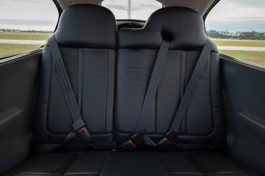 The black leather rear seats of a Cirrus SR20 aircraft cabin, with seatbelts visible.