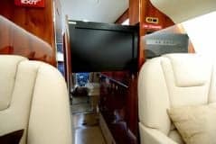 The aircraft's interior features cream-colored leather seats and a television screen.