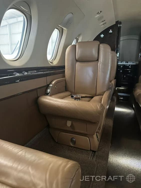 A close-up of a tan leather passenger seat with a seatbelt in the cabin of a private jet.