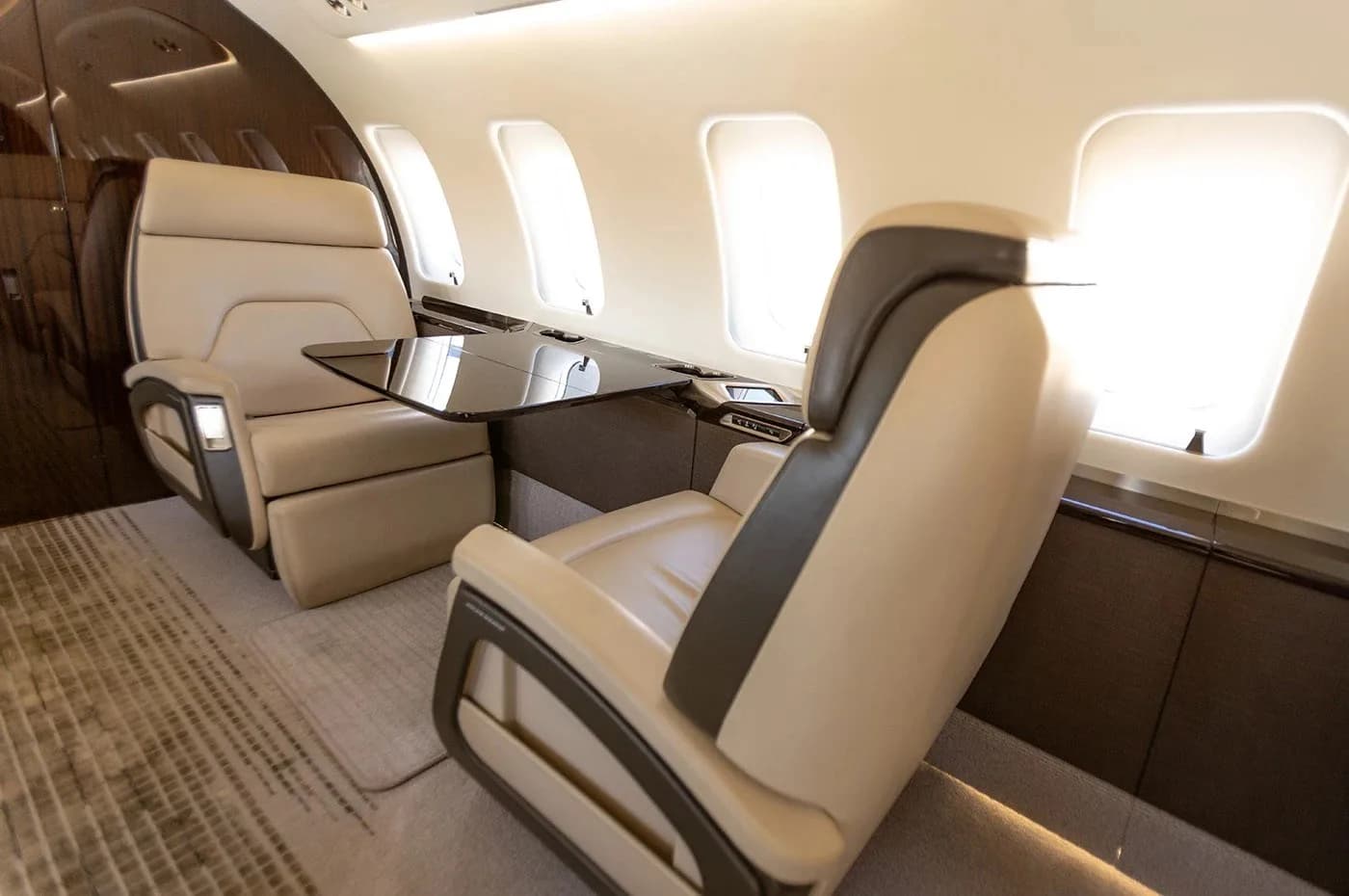 A close-up view of two beige leather seats and a small table in the luxurious cabin of a business jet.