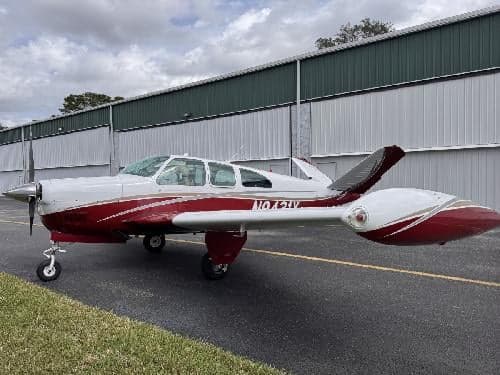 A Beechcraft Bonanza with a red and white paint scheme is parked on the tarmac.
