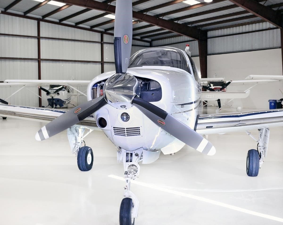 Front view of a white Beechcraft Bonanza N802PN with its engine cowling open, parked in a hangar.