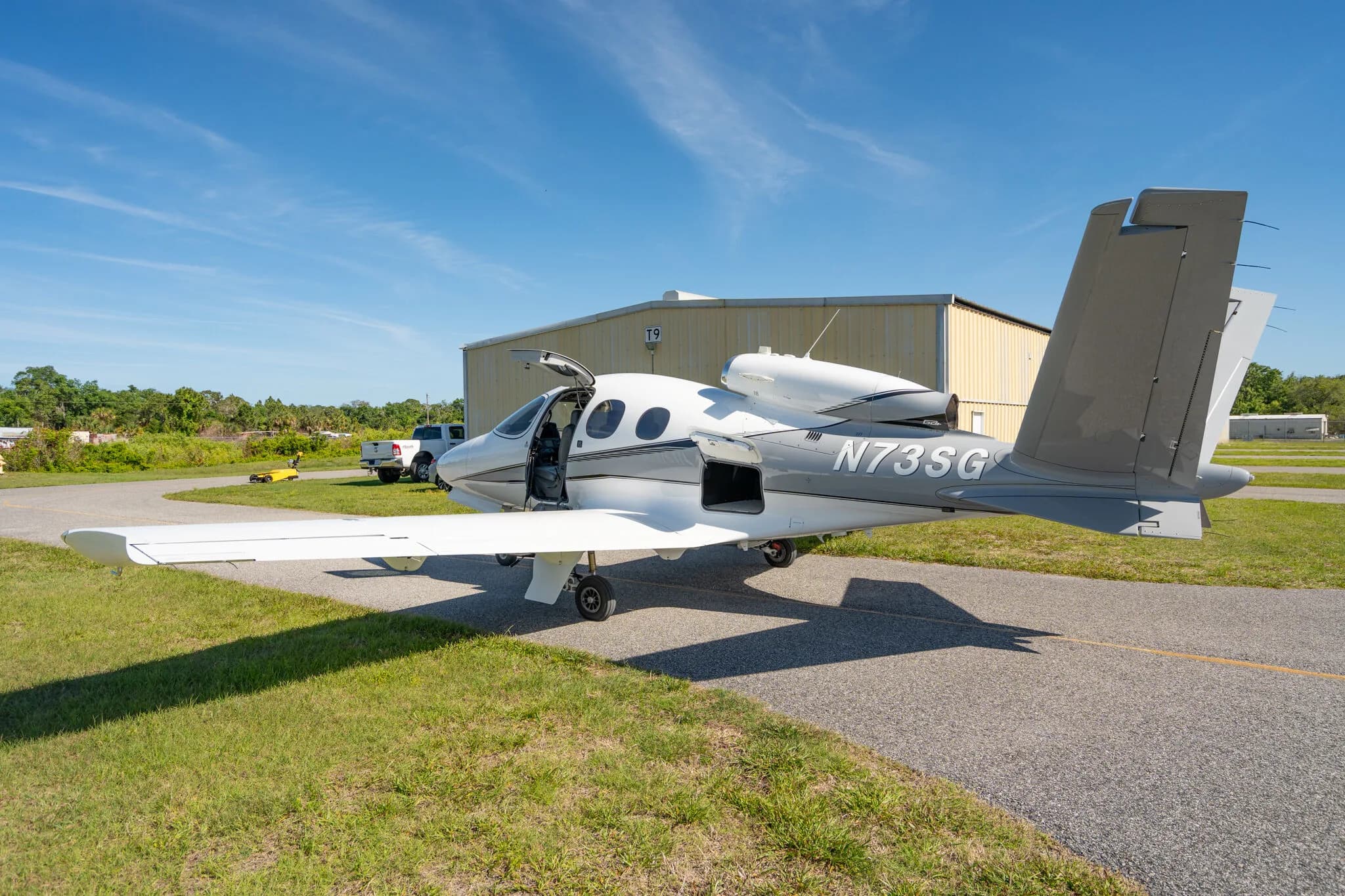 Side view of a white and grey Cirrus Vision Jet N73SG with its main door open on an airfield.