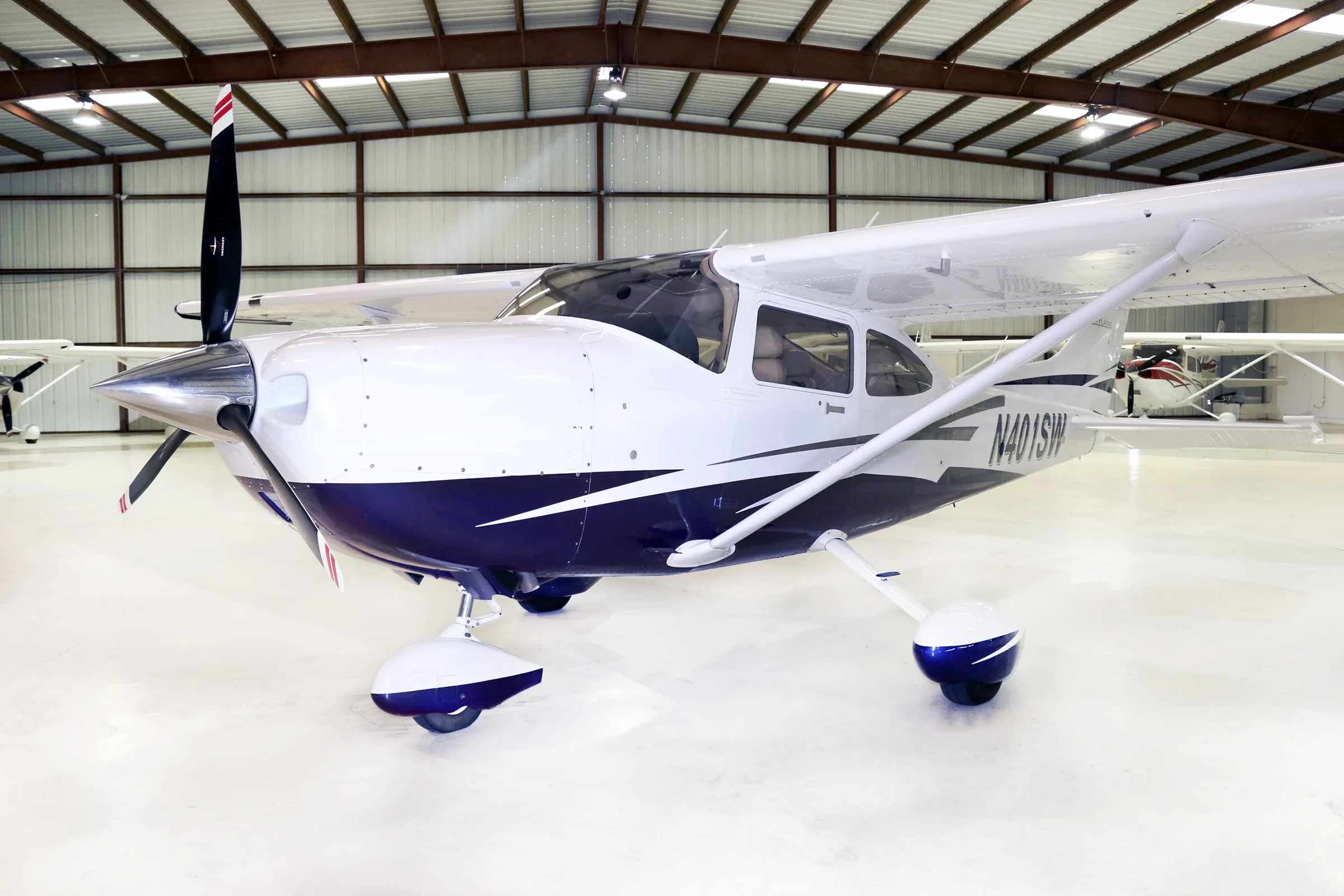 A front-left view of a white and blue Cessna Skylane aircraft with registration N401SW inside a hangar.