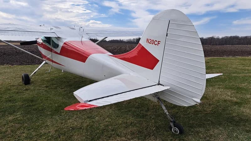 Rear view of a red and white Cessna on a grassy field.