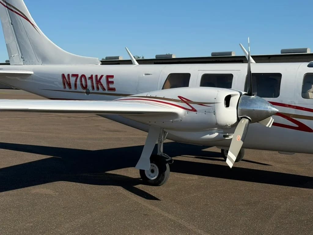 A close-up view of the right engine and rear fuselage of a white twin-engine aircraft with red and gold stripes, registration N701KE.