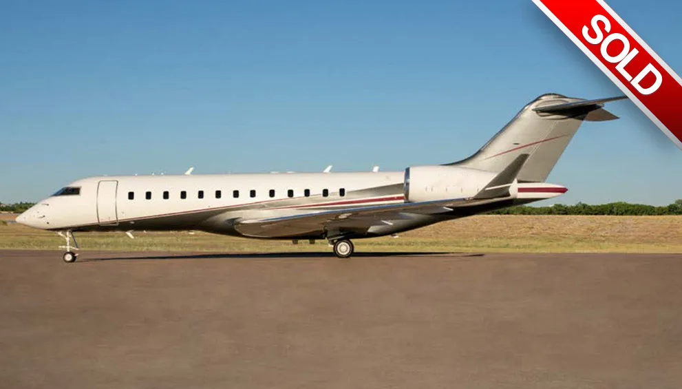 A white and grey business jet with a red stripe is parked on a tarmac under a clear blue sky.