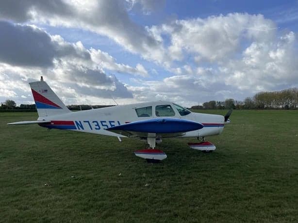 A Piper PA-28-181 Archer II aircraft, registration N735FL, is parked on a grassy field.