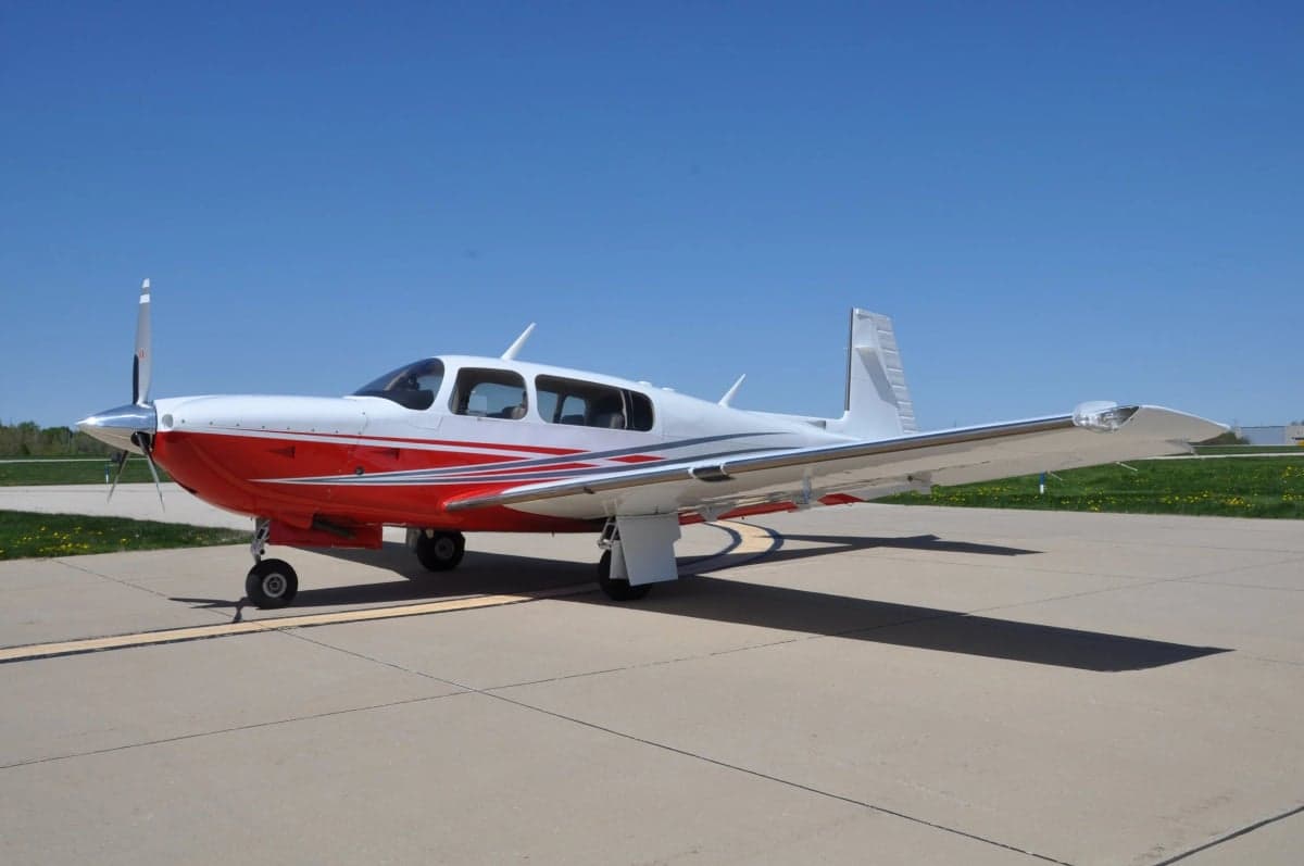A Mooney M20J aircraft with a white and red paint scheme parked on the tarmac.