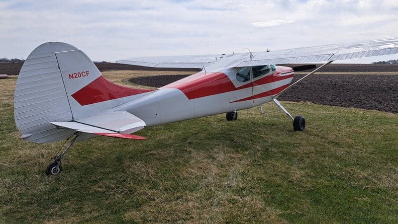 A rear view of the red and white Cessna on a grassy field.
