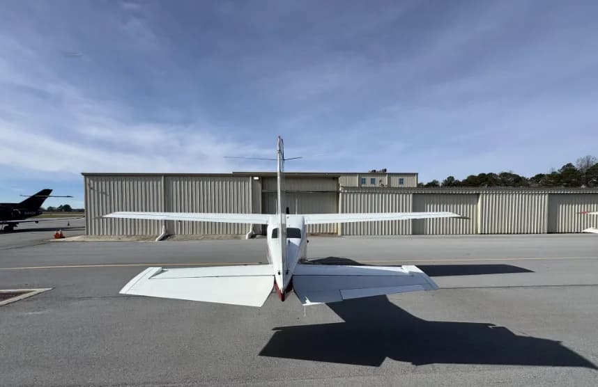 A rear view of a white Cessna 182 Skylane (N87MS) with red accents, parked on an airport tarmac.