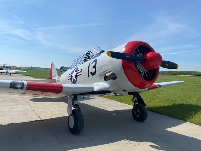 A white and red North American Aviation T-6 Texan aircraft is parked on a runway.