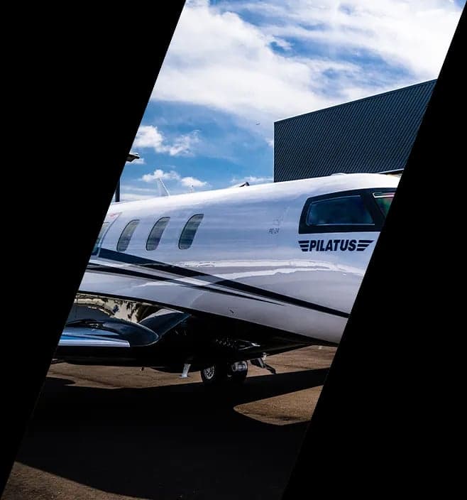 Side view of a white Pilatus PC-24 jet with black and white livery parked outside a hangar.