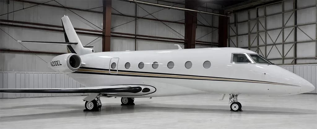 A white Gulfstream business jet with black and gold stripes is parked in a hangar, showing its left side and tail number N200EL.