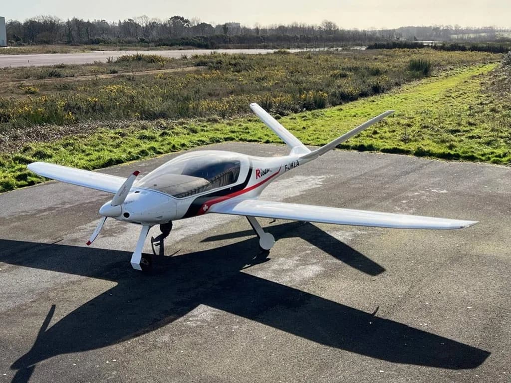 A white Risen aircraft with red and black accents and registration F-JKLA parked on an asphalt runway.