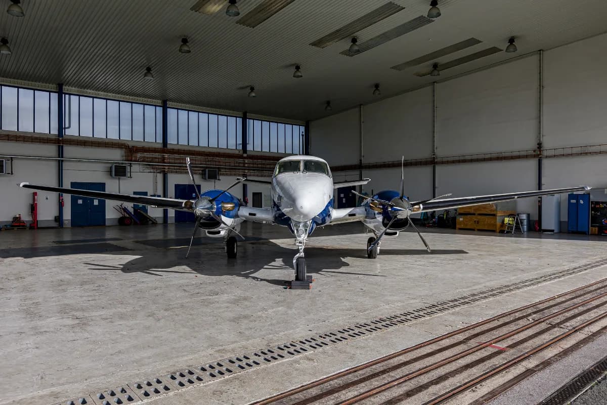 Front view of a white and blue Beechcraft King Air C90 twin-turboprop aircraft parked inside a hangar.