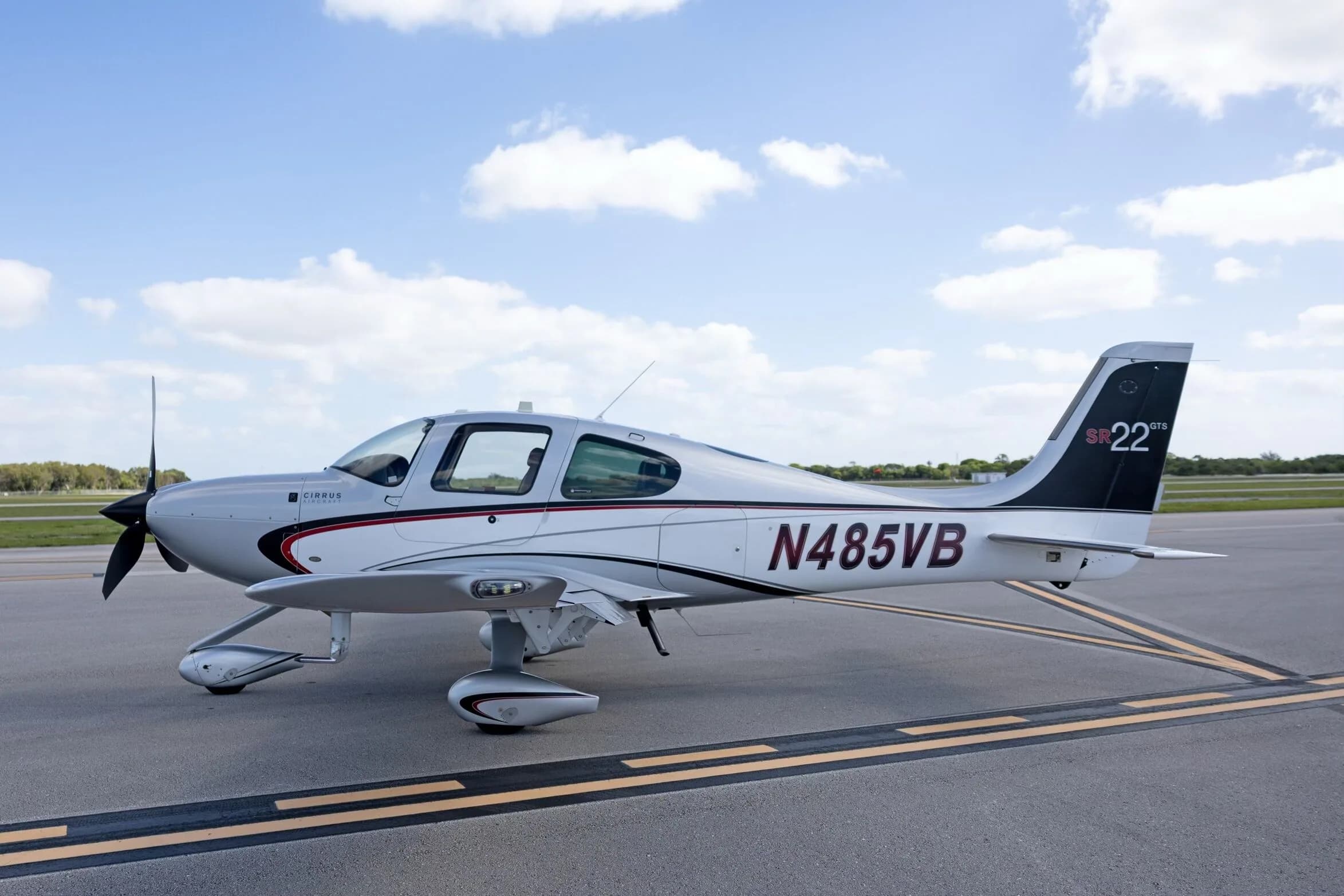 A side view of the silver Cirrus SR22 GTS aircraft N485VB, showing its sleek design and paint scheme, parked on an airfield.