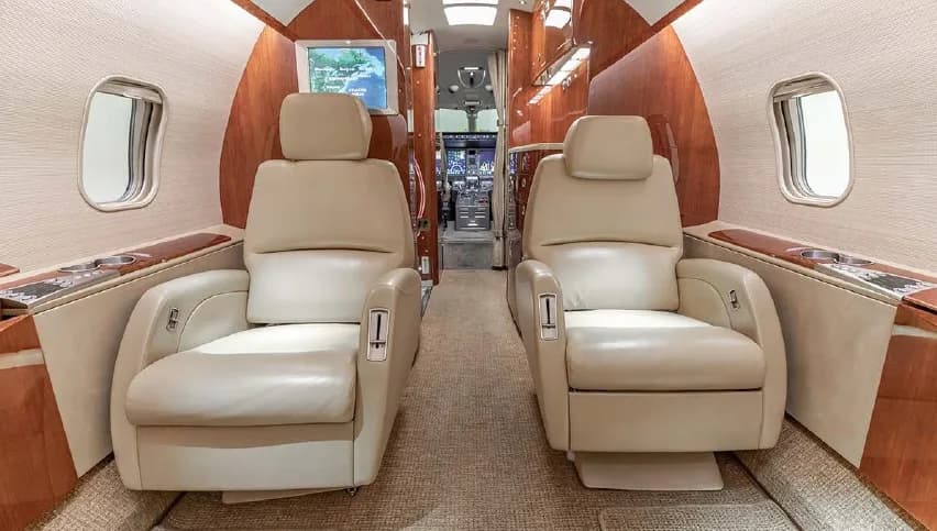 A view of the Challenger 350 cabin with beige leather seats facing the cockpit.