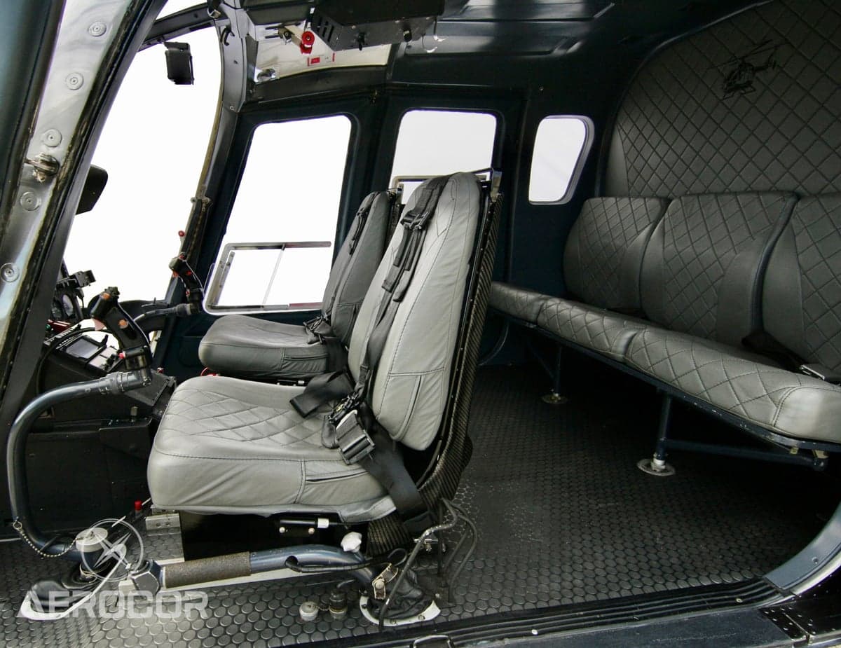 Interior view of a helicopter cabin with grey quilted seats and black floor.