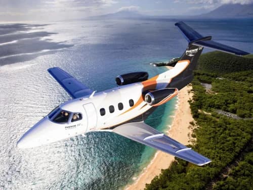A Phenom 300E flying over a tropical beach.