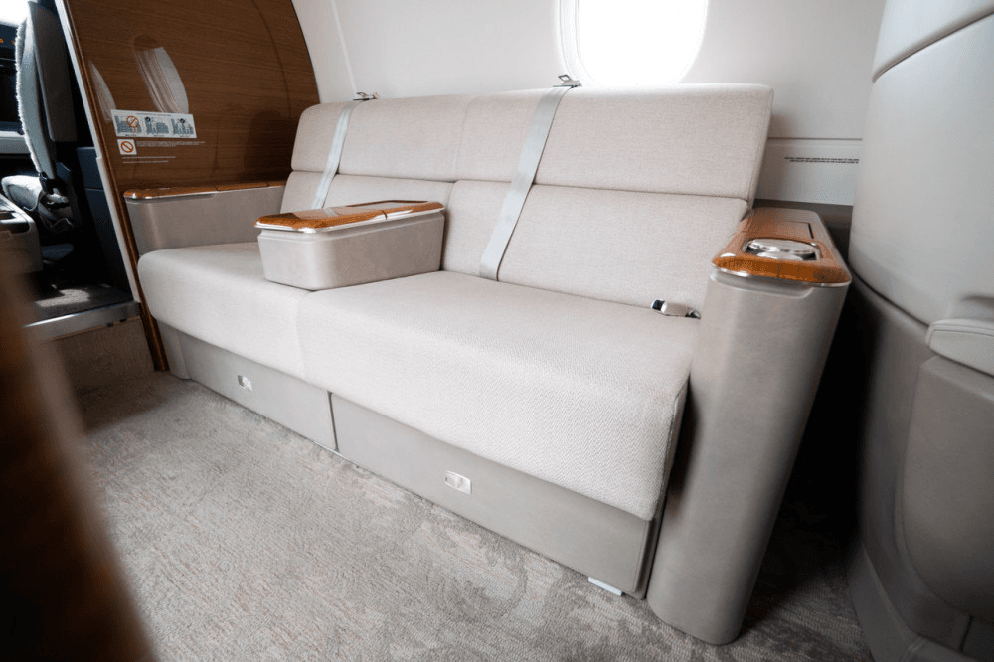 A comfortable light-colored fabric sofa seat with seatbelts and a small table in the cabin of a private jet.