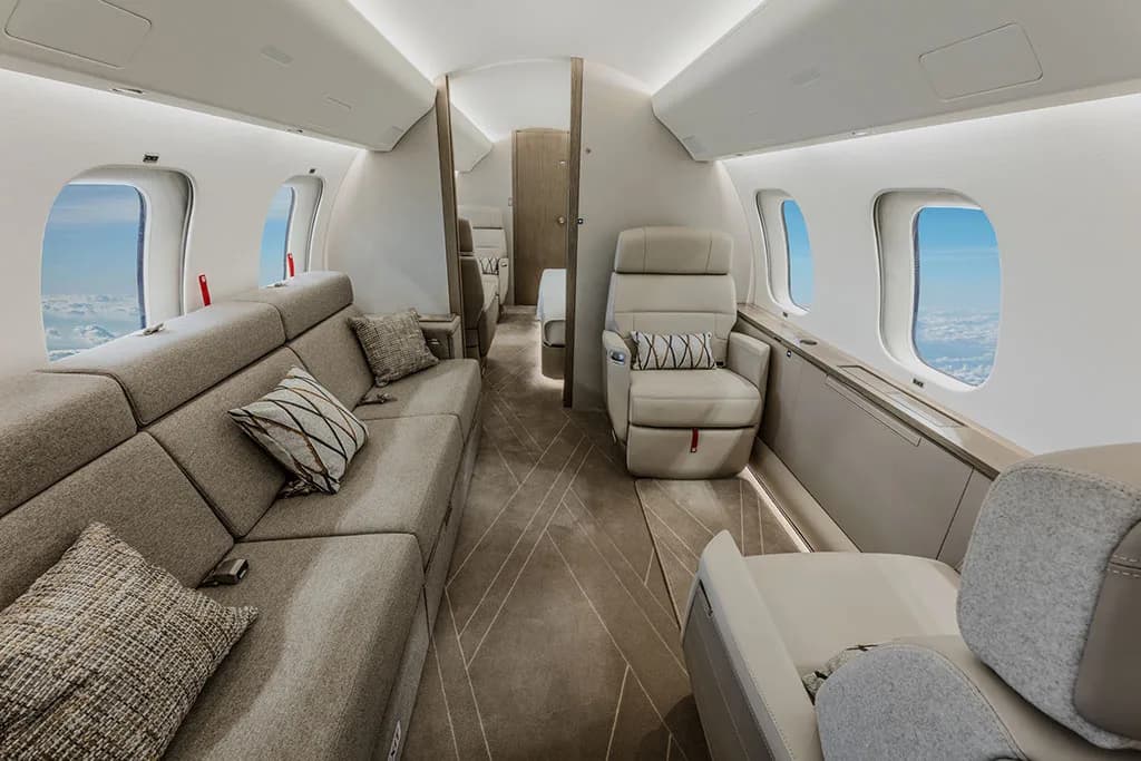 A private jet cabin with a long grey sofa on one side and individual beige seats on the other.