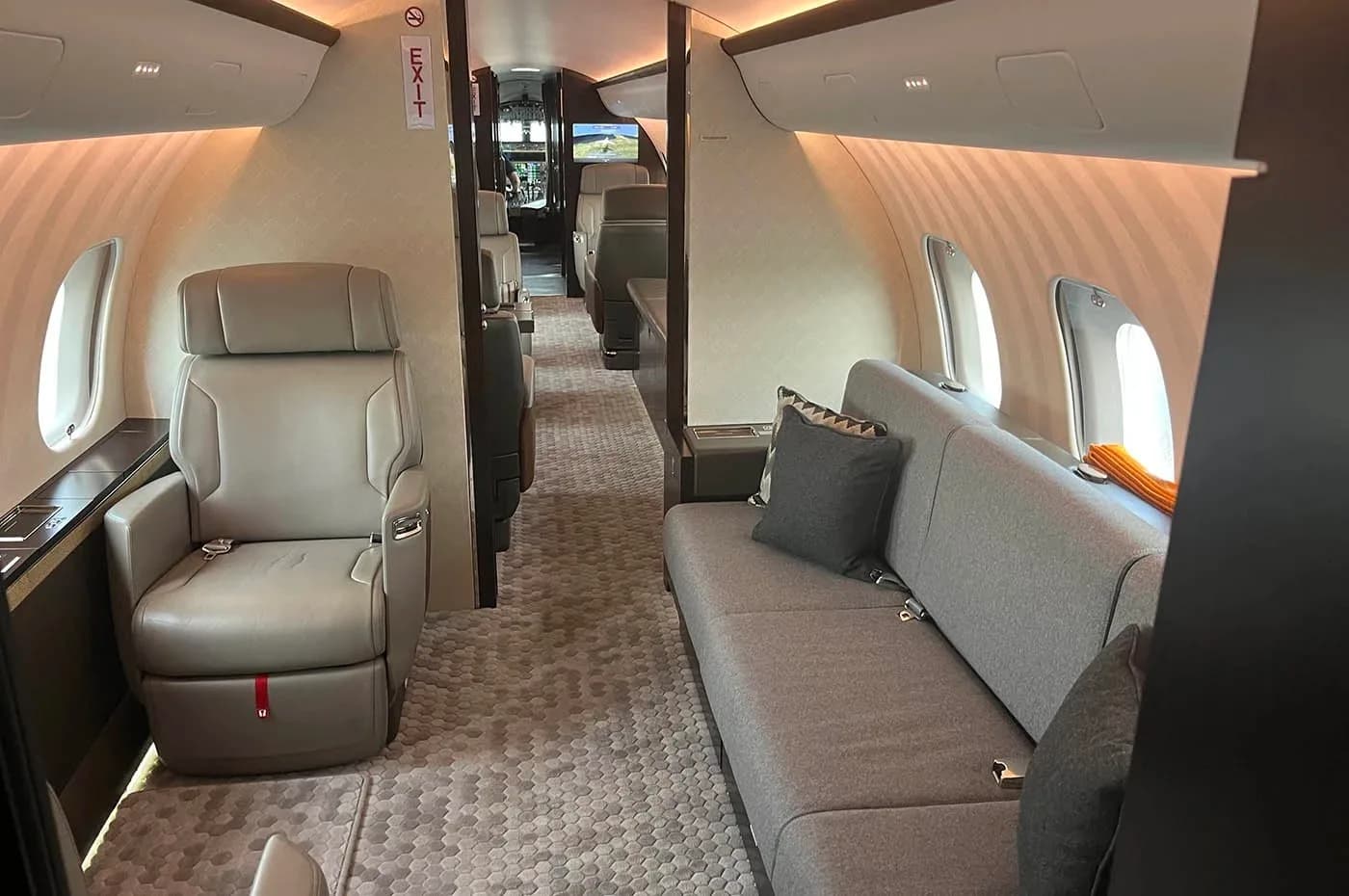 The spacious interior of a business jet cabin featuring a grey sofa and individual seats.