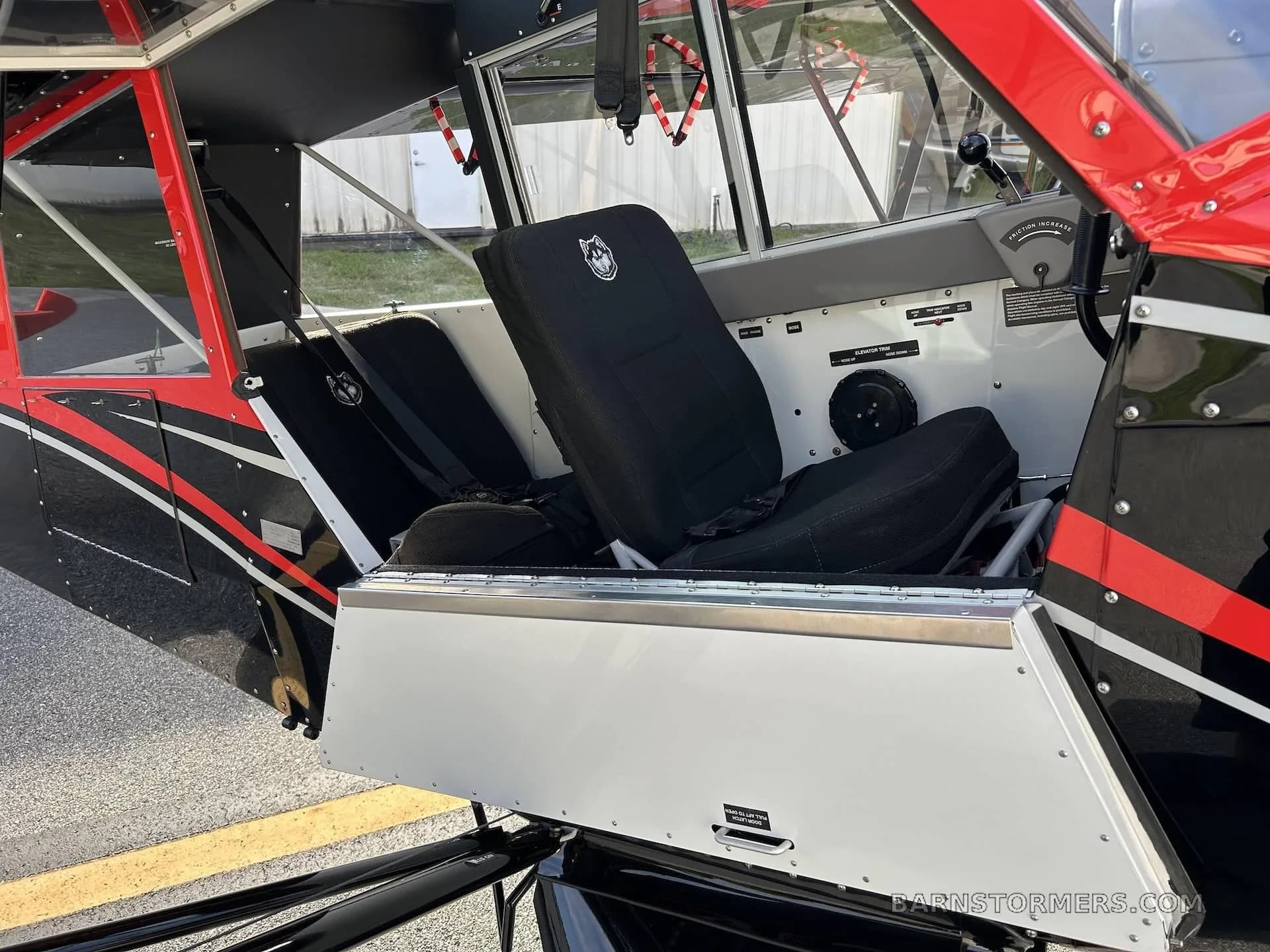 The black fabric seats and open side door of the Aviat Husky A-1C aircraft cabin are visible.