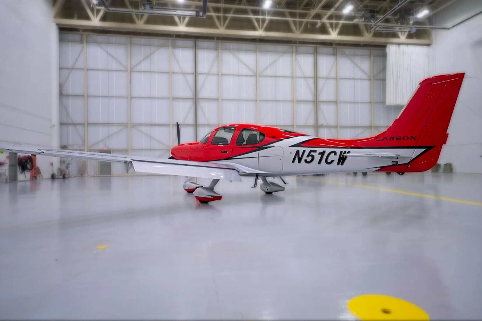 A side view of a red and white Cirrus SR22 aircraft with registration N51CW in a hangar.