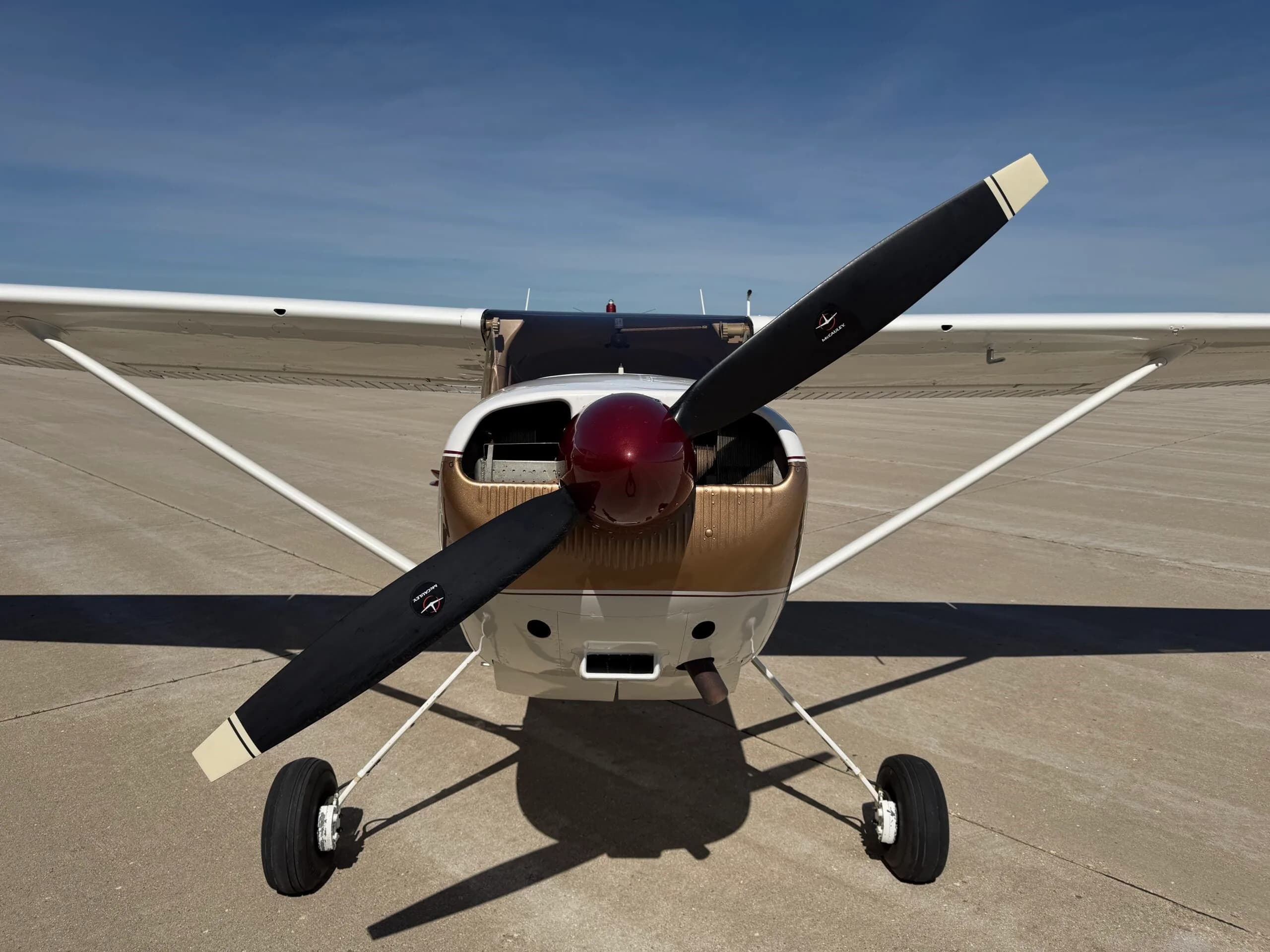 Head-on view of a white, gold, and maroon Cessna 172 on an airfield.